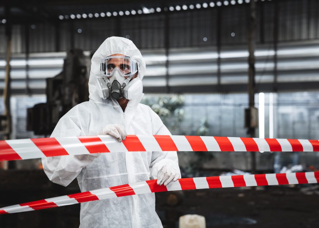 A worker in a hazmat suit behind caution tape