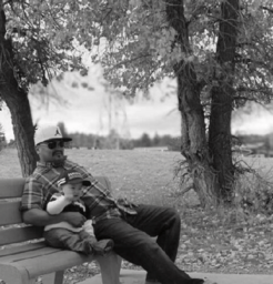 Man lounging on a bench with a baby beside him.